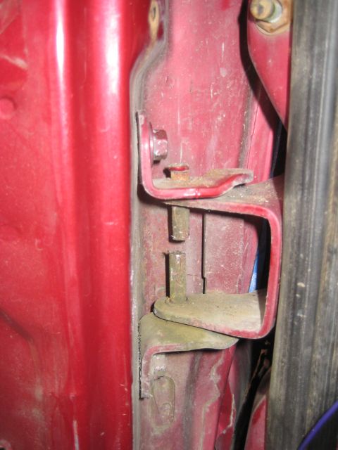 1995 Ford Bronco - The door hinge assembly on a red vehicle shows signs of wear and dust accumulation.