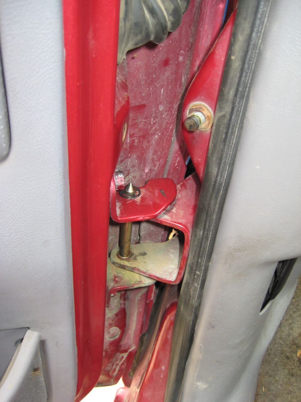 Close-up of a red vehicle door hinge mechanism with visible bolts and metal components