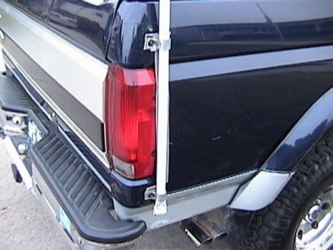 1995 Ford Bronco - Close-up of the driver-side rear corner of a dark blue two-tone full-size Ford Bronco, showing the red vertical taillight, silver lower bod…