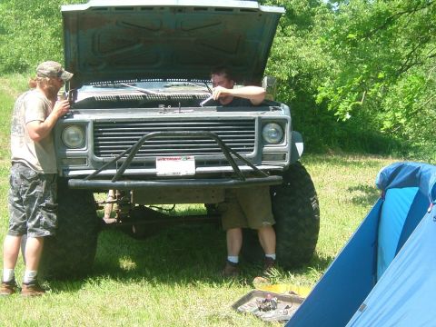 1978 Chevrolet C/K Pickup - Two men work on a lifted gray truck with its hood open, a blue tent pitched to the side.