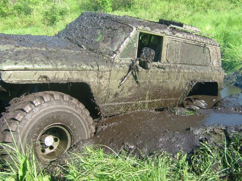 1978 Chevrolet C/K Pickup - An olive green off-road vehicle is deeply mired in thick mud, with only its front wheel partially visible above the mire.