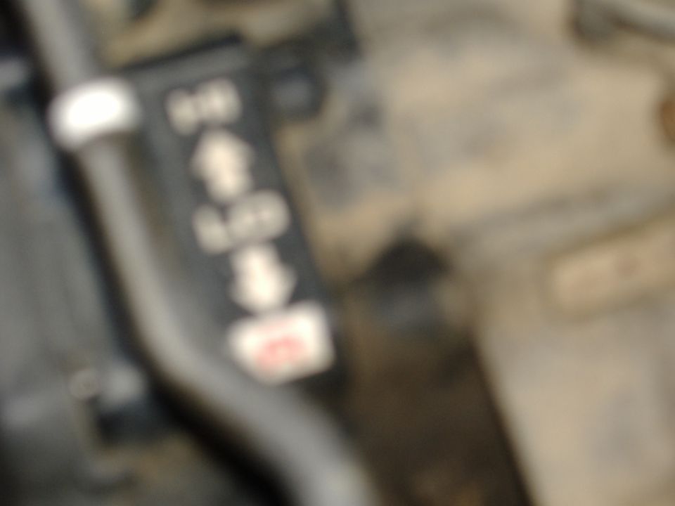 Blurry close-up of a black gear selector lever with an arrow-marked shift pattern label