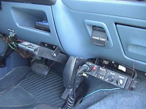 1995 Ford Bronco - Interior under-dash view of a blue-gray Ford truck cab showing a CB radio mounted upside-down on a fabricated black bracket bolted beneath…