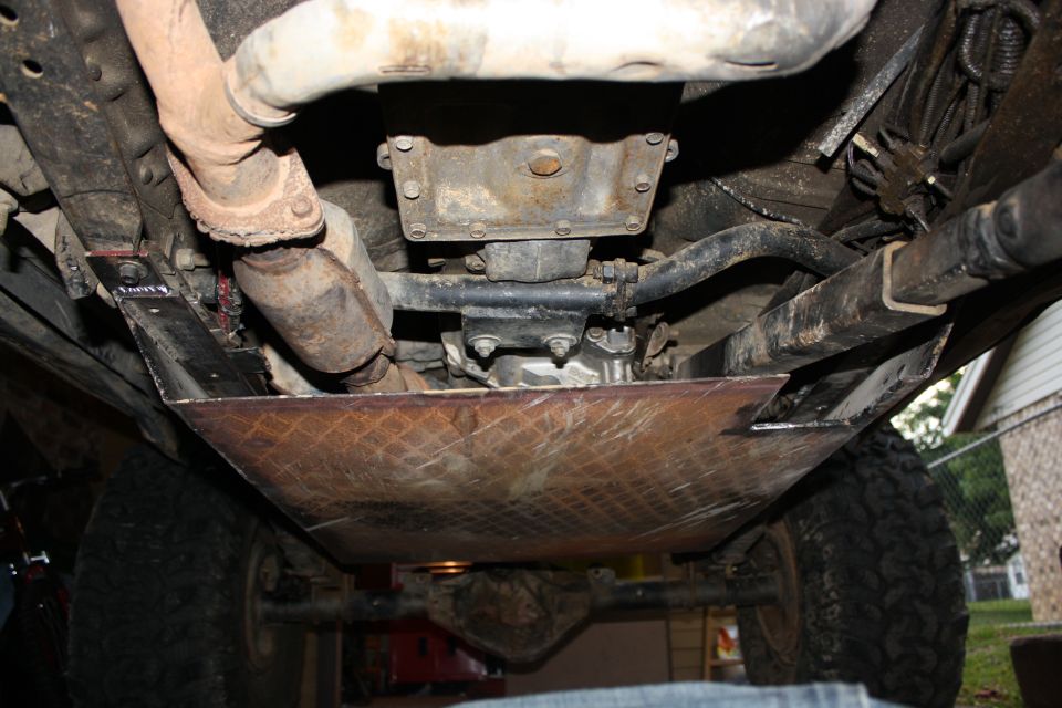 Underside view of a vehicle's drivetrain and exhaust system, showing a skid plate installed
