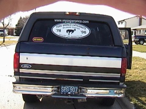 1995 Ford Bronco - Straight-on rear view of a dark blue full-size Ford Bronco in a residential driveway, showing the chrome-trimmed tailgate with Ford oval, c…