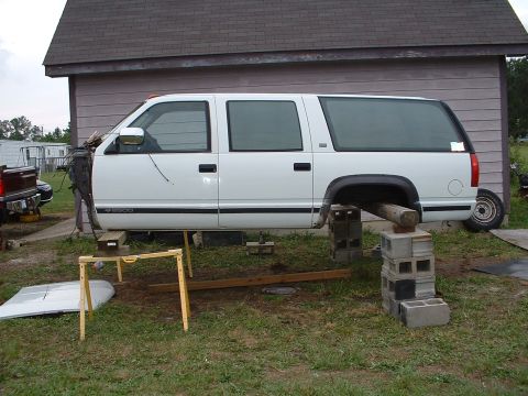 1994 GMC Suburban - White 1995 Chevrolet Suburban missing its front end, elevated on cinder blocks for repairs.