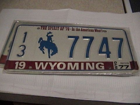 1995 Ford Bronco - A vintage 1977 Wyoming license plate reading 13 7747 in a chrome frame, laid on white paper. The white plate carries the blue bucking-horse…