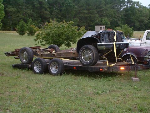 1994 GMC Suburban - A disassembled vehicle chassis and front clip are loaded onto a trailer, with another vehicle partially visible.