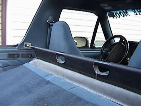 1995 Ford Bronco - Interior view over a gray carpeted rear cargo area showing a padded black sport/roll bar mounted behind gray cloth bucket seats, with the s…