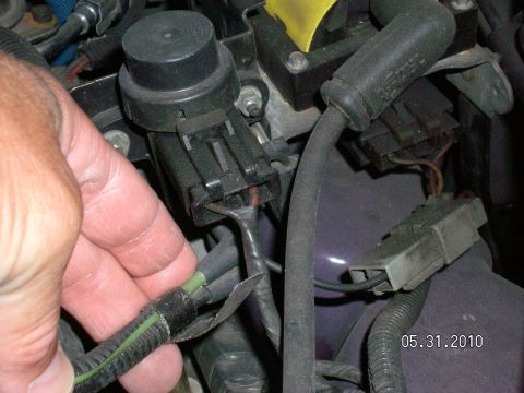 1996 Ford Bronco - Close-up of a hand disconnecting a wire from a vehicle's engine wiring harness.