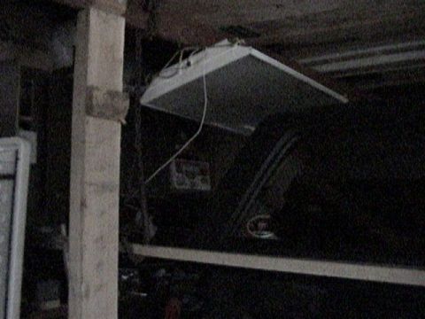 1995 Ford Bronco - Very dark garage interior showing a removable hardtop hoisted up and suspended from the ceiling joists by cables next to a wooden post. The…