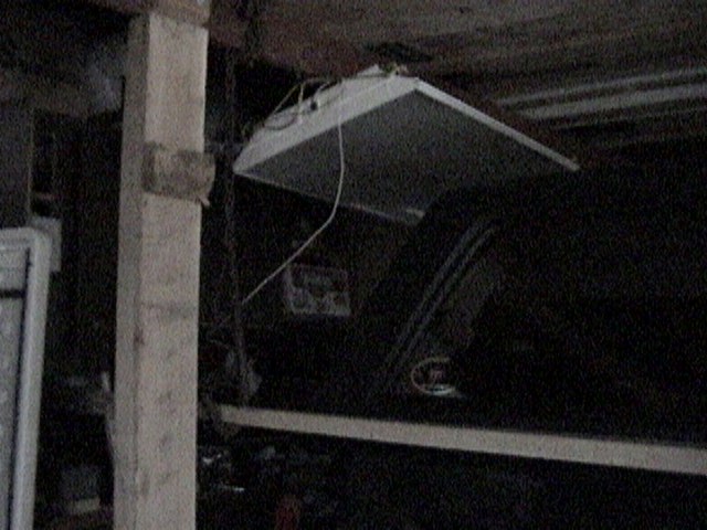 Removable hardtop hoisted to garage ceiling by cables in a dark garage