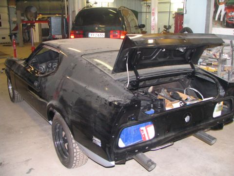 1971 Ford Mustang - A black 1971 Ford Mustang is shown in a garage with its trunk open, revealing stored items.
