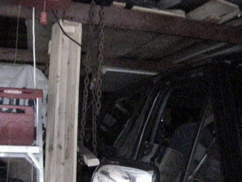 1995 Ford Bronco - Dim garage interior shot of a hardtop being lifted off an SUV with a chain hoist running down from the wooden ceiling joists; the rear side…