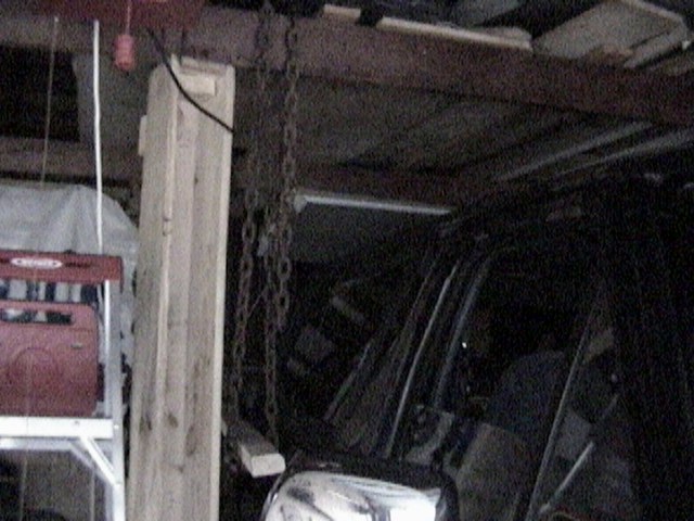 Chain hoist rigged to lift a hardtop off an SUV in a dark garage