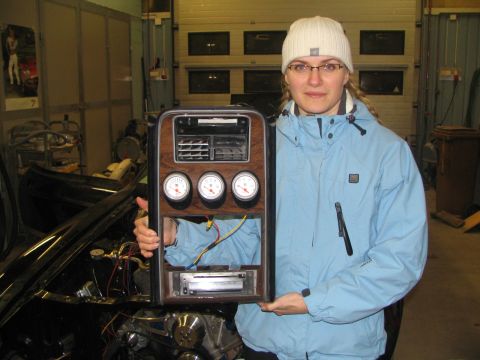 1971 Ford Mustang - A woman holds a vintage dashboard part gauges, vents, and a radio.