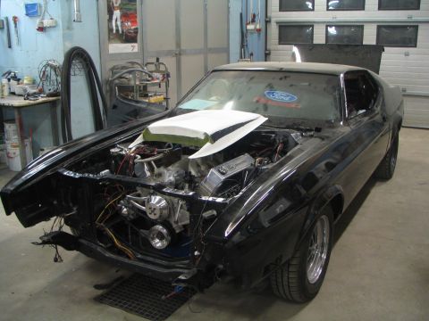 1971 Ford Mustang - A black 1971 Ford Mustang is shown in a garage with its hood open, revealing the engine and various components.