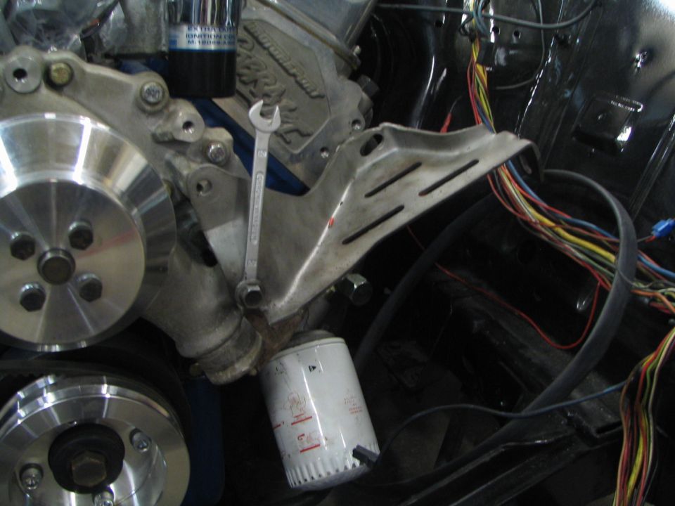Close-up of engine bay showing pulleys, oil filter, and wiring harness. A wrench is attached to a bracket