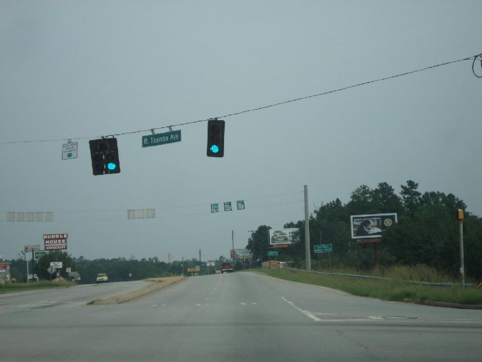 Roadway intersection with traffic lights, street signs, and billboards under an overcast sky