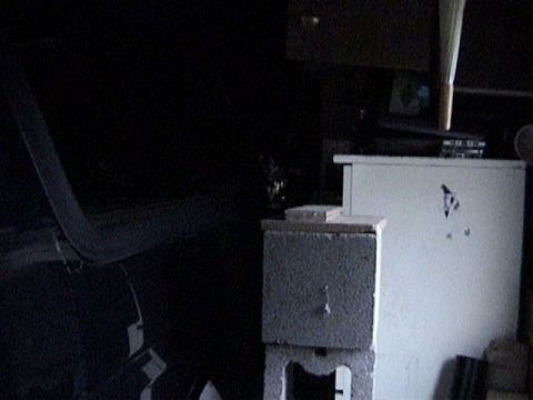 1995 Ford Bronco - Very dark garage interior shot showing the curved edge of a removed dark fiberglass hardtop leaning at left, propped near a white metal cab…