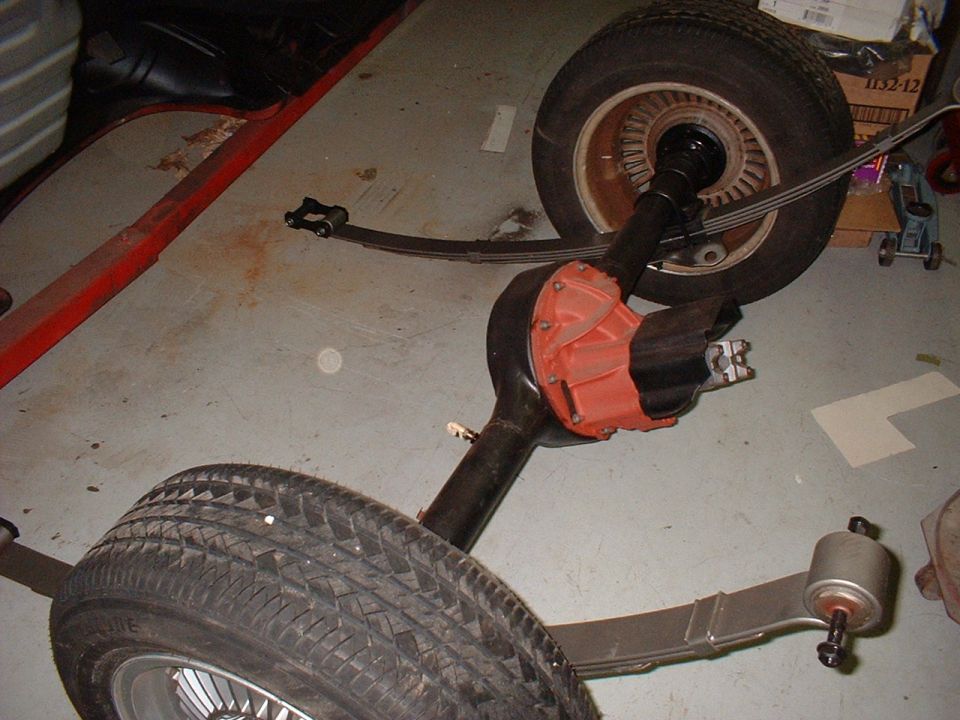 Rear axle housing with orange differential center and leaf springs on garage floor