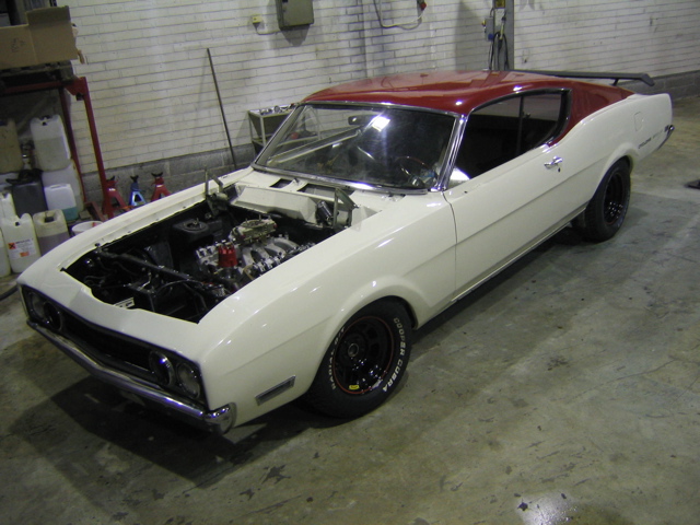 White 1969 Mercury Cyclone coupe with red roof and exposed engine, viewed from the front-right