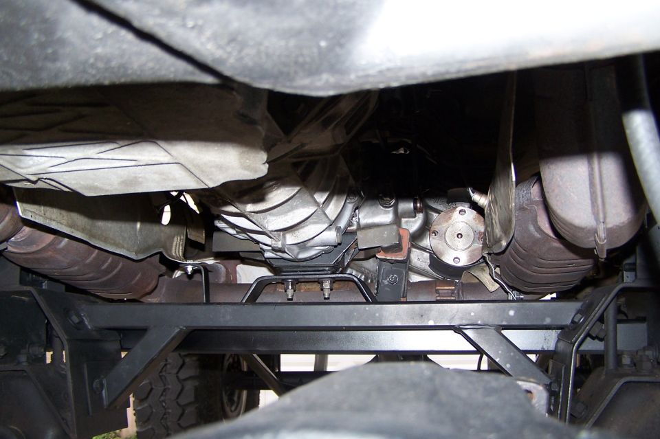 Underside view of a vehicle's transmission, driveshaft, and exhaust system. A watermark reads SUPERMOTORS