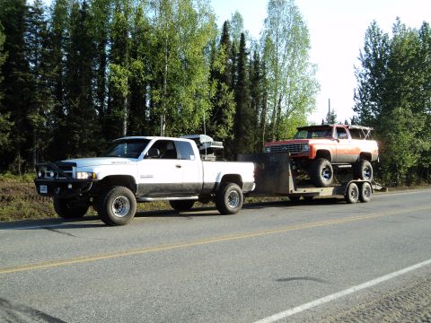 1990 Chevrolet Suburban - A white pickup truck tows a red SUV on a trailer down a highway.
