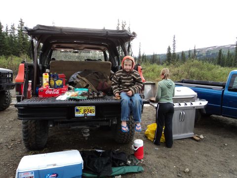 1990 Chevrolet Suburban - A family is set up for a barbecue outdoors with a cooler and grill next to their vehicles.