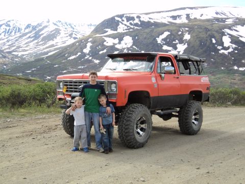 1990 Chevrolet Suburban - Three boys pose with a heavily modified orange pickup truck in a mountainous landscape.
