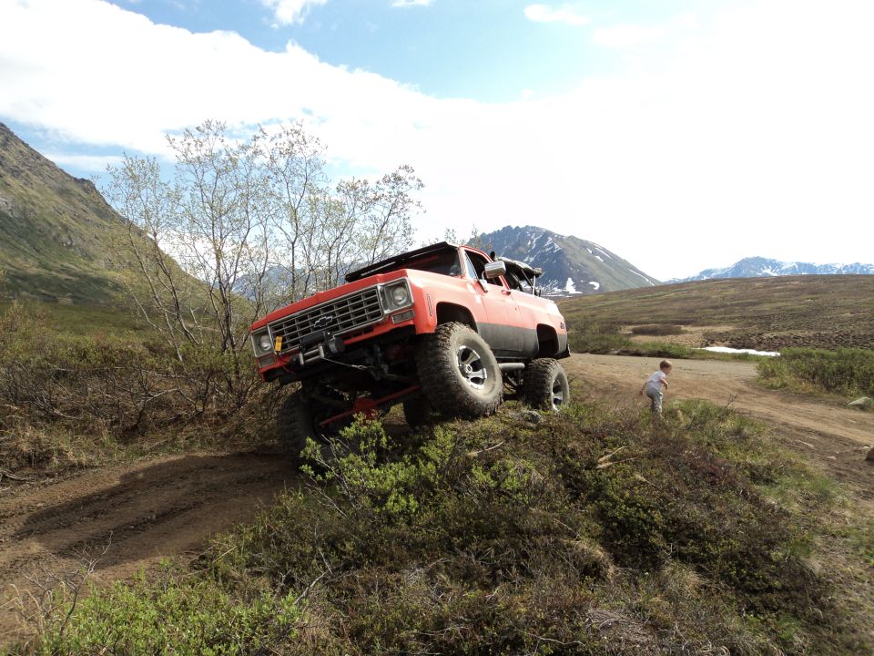 Red off-road truck with large tires climbing a dirt hill, mountains in background