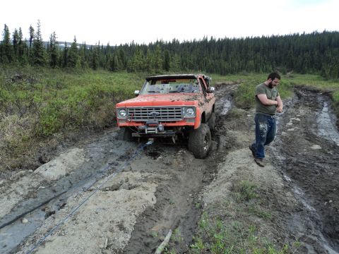 1990 Chevrolet Suburban - A man watches as his orange truck is stuck deep in the mud on a trail.
