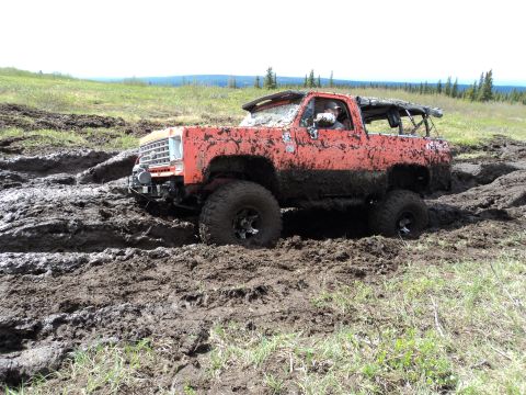 1990 Chevrolet Suburban - This heavily muddied orange pickup truck is struggling to navigate a challenging off-road terrain.