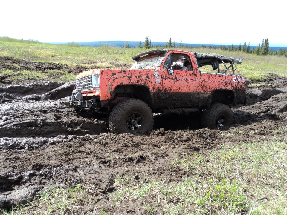 Mud-covered orange pickup truck with a roll bar, stuck in deep mud