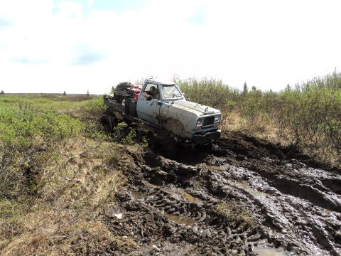 1990 Chevrolet Suburban - A white pickup truck navigates a challenging muddy terrain, with its tires deep in the mire.