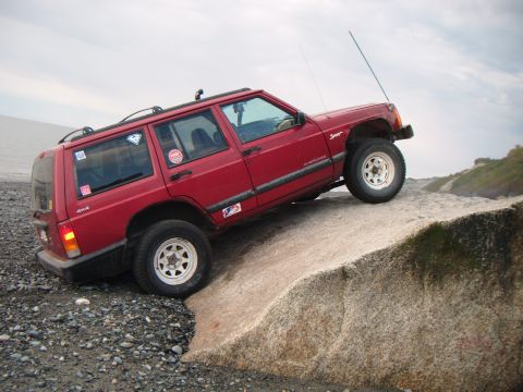 1998 Jeep Cherokee - A red 1998 Jeep Cherokee navigates a rocky incline near the coast.