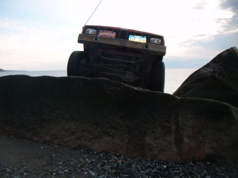 1998 Jeep Cherokee - A red 1998 Jeep Cherokee is positioned on rocks near the water, with its front grille and headlights visible.