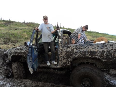 1990 Chevrolet Suburban - A muddy truck with people and a dog is stuck in the mud.