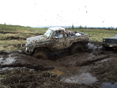 1990 Chevrolet Suburban - Off-road vehicles navigate a challenging muddy terrain, with one truck deeply mired.