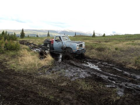 1990 Chevrolet Suburban - A lifted pickup truck navigates a challenging muddy terrain with a scenic, hilly background.