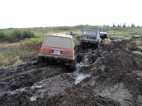 1990 Chevrolet Suburban - Multiple off-road vehicles navigate a challenging muddy terrain, with a red Jeep Cherokee prominently featured.