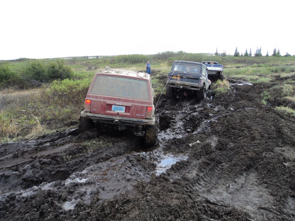 Red Jeep Cherokee rear view, stuck in mud with other vehicles behind
