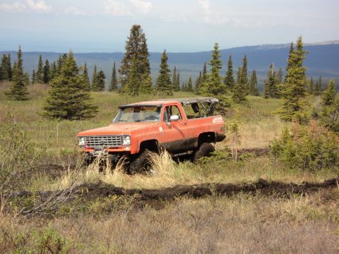 1990 Chevrolet Suburban - This off-road SUV navigates a muddy trail surrounded by trees and hills.