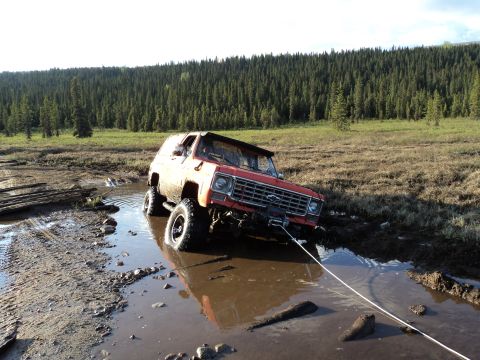 1990 Chevrolet Suburban - Off-road SUV is stuck in a muddy puddle with a forest in the background.