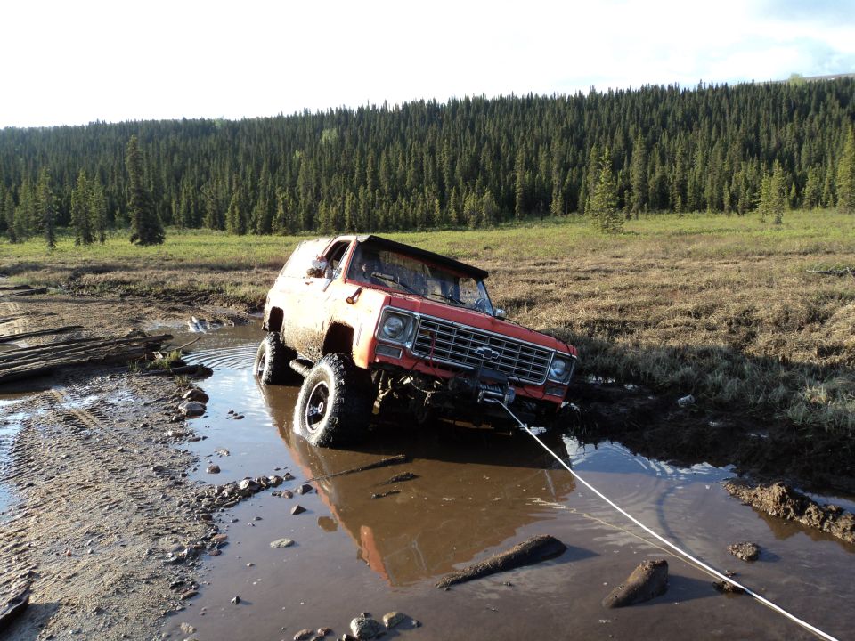 red off-road SUV stuck in mud, being pulled by a rope