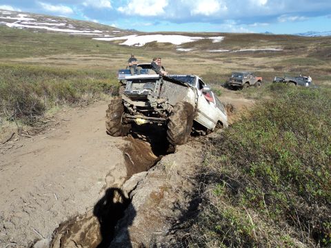 1990 Chevrolet Suburban - Vehicles struggle through a challenging muddy terrain with snow-capped hills in the background.