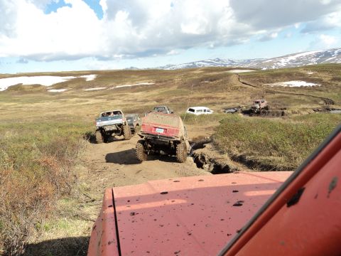 1990 Chevrolet Suburban - Several off-road vehicles traverse a challenging muddy terrain under a cloudy sky.