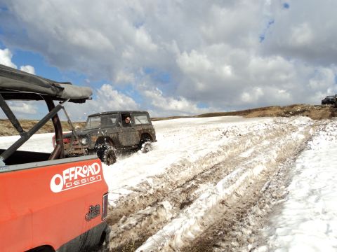 1990 Chevrolet Suburban - Two off-road vehicles navigate a snowy, muddy terrain under a cloudy sky.