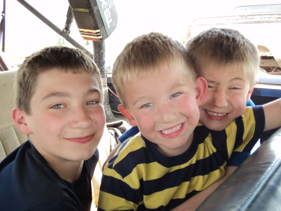 Three young boys smiling for a photo inside what appears to be a vehicle
