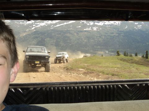1990 Chevrolet Suburban - A group of off-road vehicles navigates a dusty trail in a mountainous landscape.
